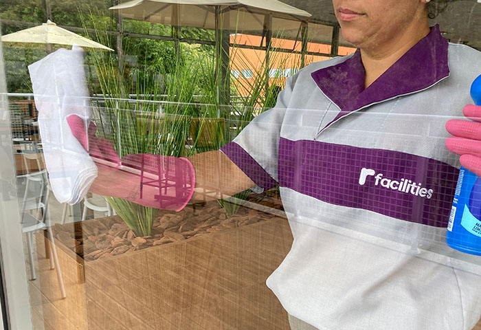Colaboradora da R Facilities realizando limpeza de vidros com luvas e produtos padronizados, demonstrando controle de insumos e qualidade operacional