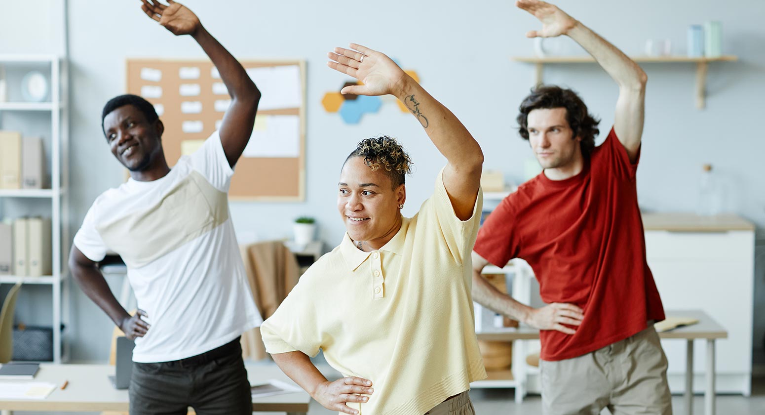 Colaboradores em pé, realizando exercício de ginástica laboral no escritório